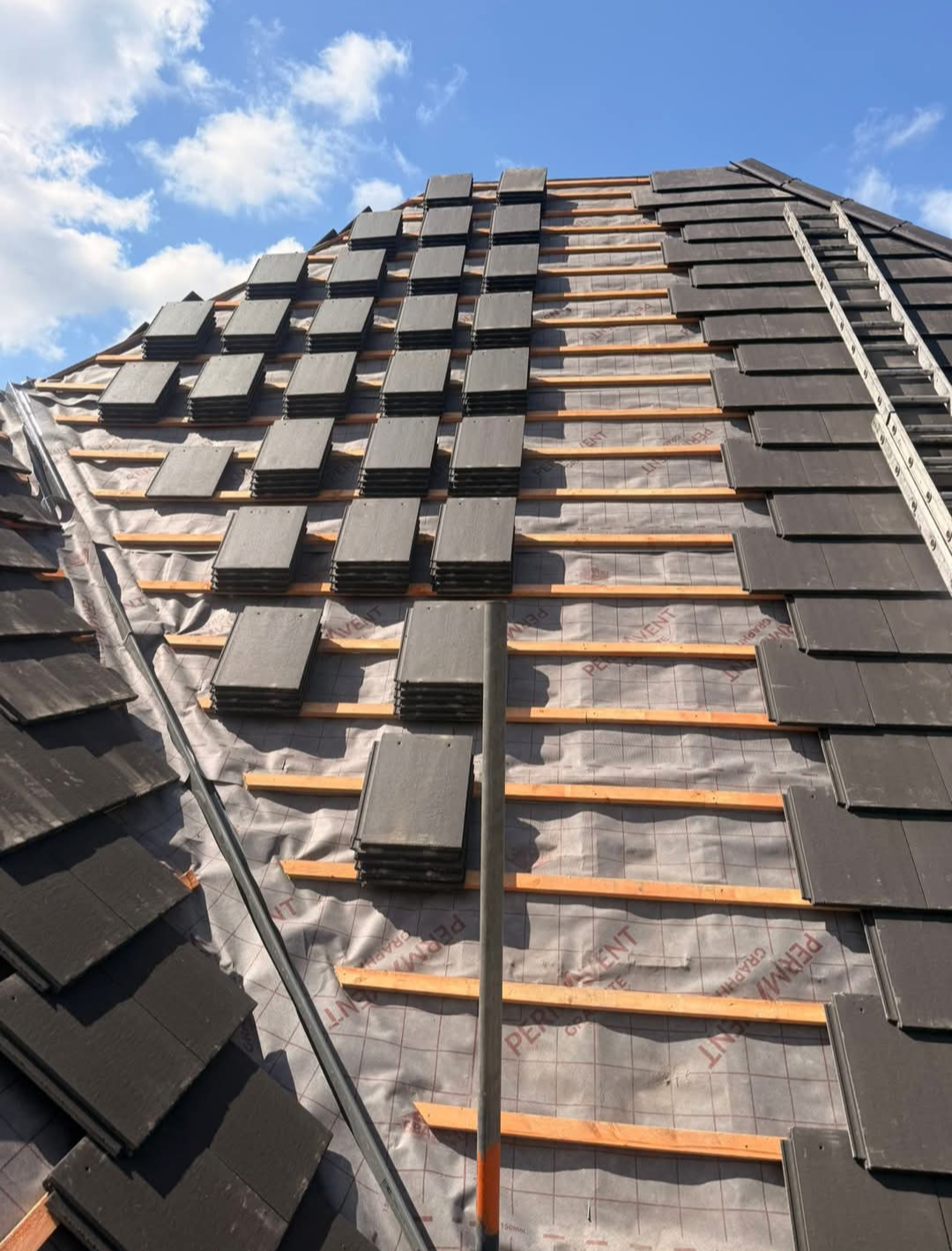 Roof under construction with battens and stacked dark roof tiles ready for fitting.