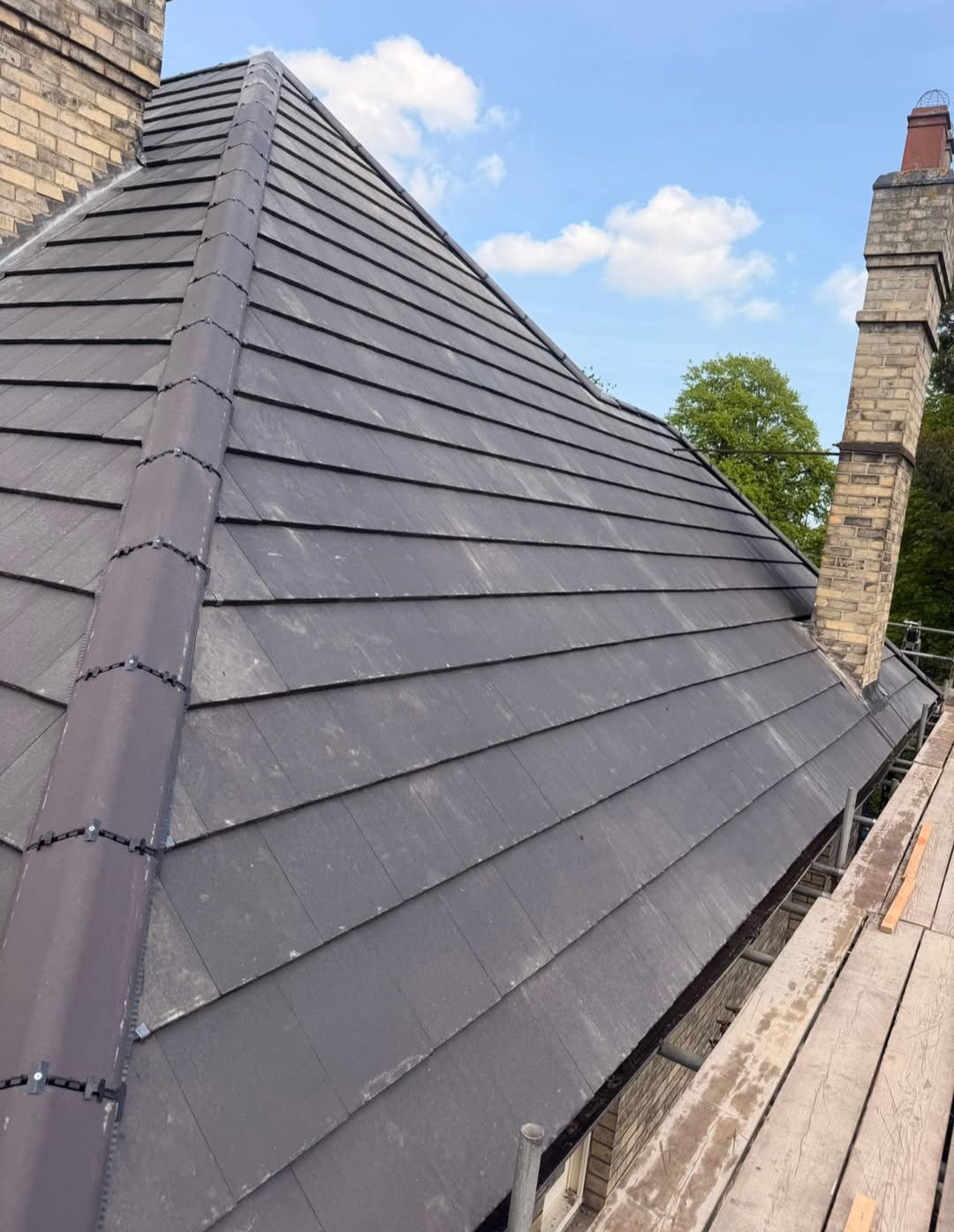 Completed dark slate-style roof on a house with chimney stacks.